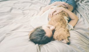 A girl with a poodle dog sleeping on the bed