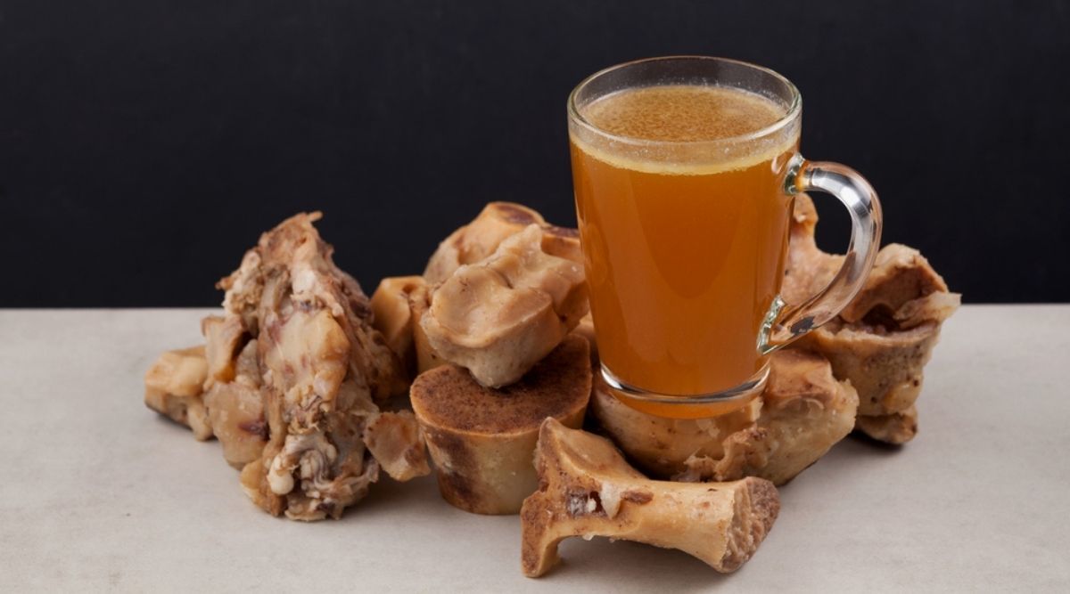 Cup of homemade bone broth is placed on boiled beef bones, which contain the necessary amino acids for a dog's body
